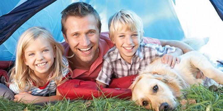 A father with his young son & daughter all lying in front of a tent with a Golden Retriever dog