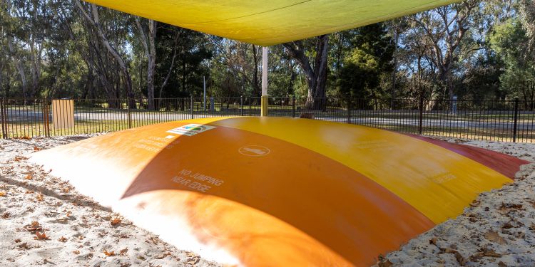A large jumping pillow surrounded by white sand with a large yellow shade sail overhead.